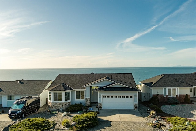 view of front of house featuring a garage, stone siding, a water view, and driveway