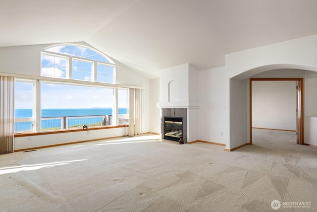 unfurnished living room with baseboards, a tile fireplace, lofted ceiling, a water view, and carpet flooring