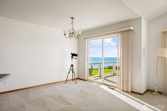 carpeted empty room with a chandelier, a water view, visible vents, and baseboards