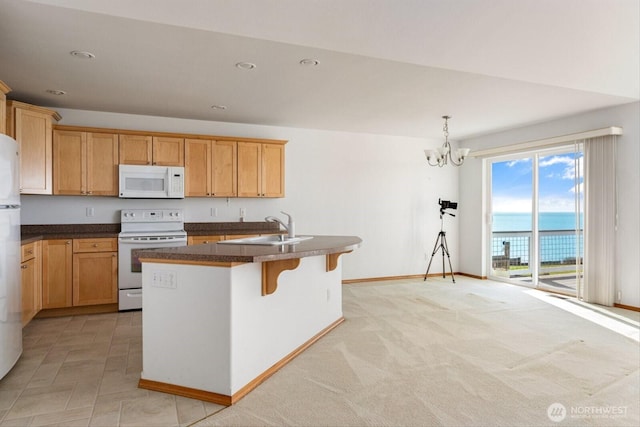 kitchen featuring white appliances, a sink, an island with sink, dark countertops, and an inviting chandelier