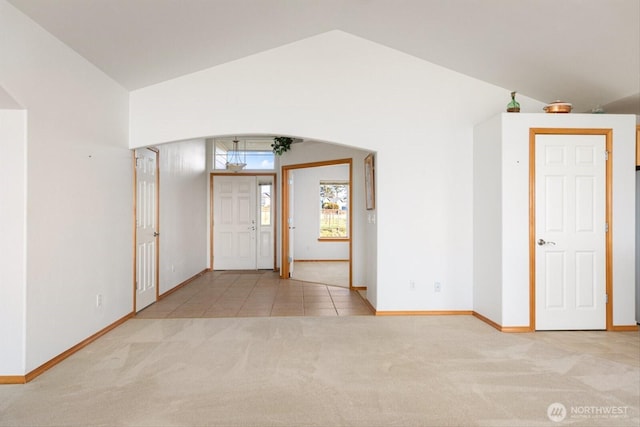 tiled foyer entrance with carpet floors, arched walkways, and vaulted ceiling