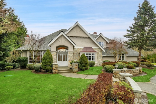 view of front facade featuring french doors, roof with shingles, stucco siding, a front lawn, and a chimney