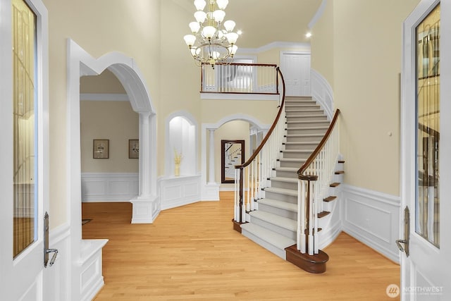 foyer entrance featuring arched walkways, light wood-type flooring, a decorative wall, and stairway