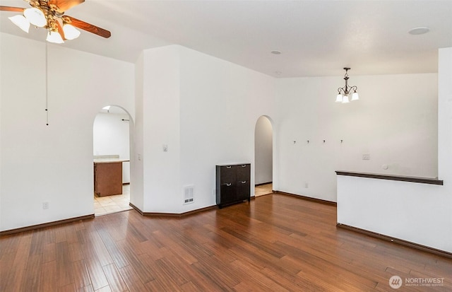 spare room with arched walkways, visible vents, wood finished floors, baseboards, and ceiling fan with notable chandelier