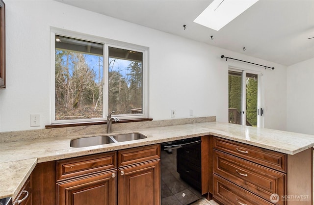 kitchen featuring a skylight, a sink, light stone countertops, dishwasher, and a peninsula