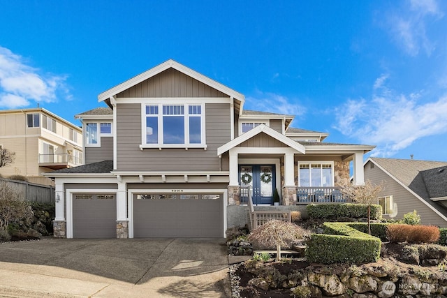 view of front of property featuring french doors, a porch, an attached garage, stone siding, and driveway