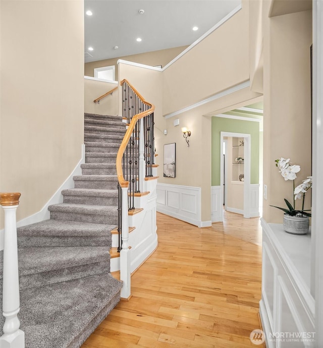 staircase with a wainscoted wall, recessed lighting, a decorative wall, a towering ceiling, and wood finished floors