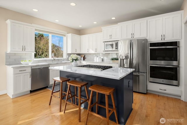 kitchen featuring stainless steel appliances, a breakfast bar, a kitchen island, light wood-style floors, and white cabinets