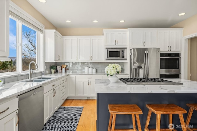 kitchen featuring a breakfast bar, backsplash, appliances with stainless steel finishes, white cabinetry, and a sink