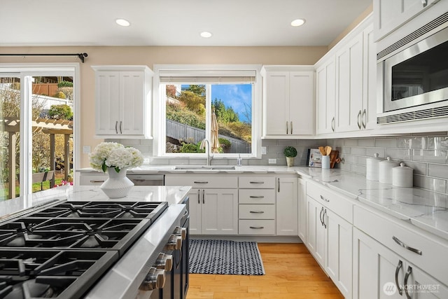 kitchen with light wood finished floors, white cabinetry, stainless steel appliances, and a sink