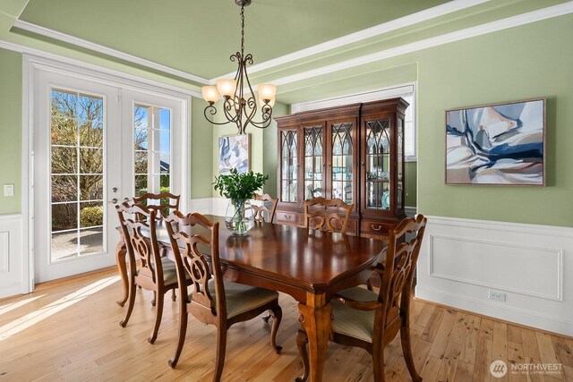 dining space with a wainscoted wall, light wood-style flooring, crown molding, and french doors