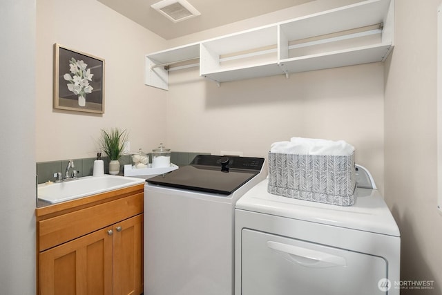 clothes washing area featuring visible vents, independent washer and dryer, a sink, and cabinet space