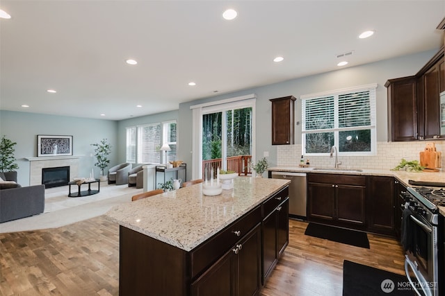 kitchen featuring light stone counters, backsplash, appliances with stainless steel finishes, a glass covered fireplace, and a sink