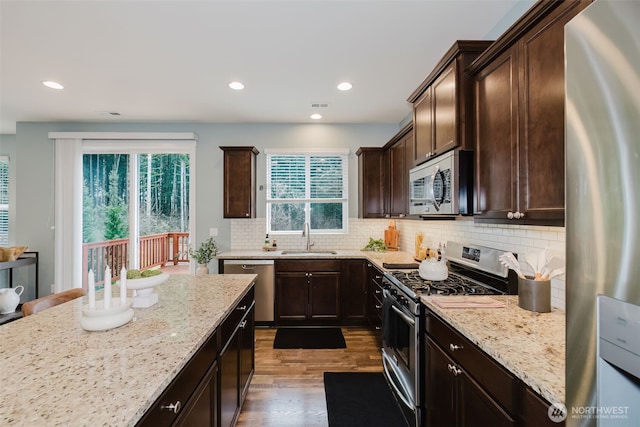 kitchen with light stone counters, dark wood-style floors, appliances with stainless steel finishes, dark brown cabinetry, and a sink