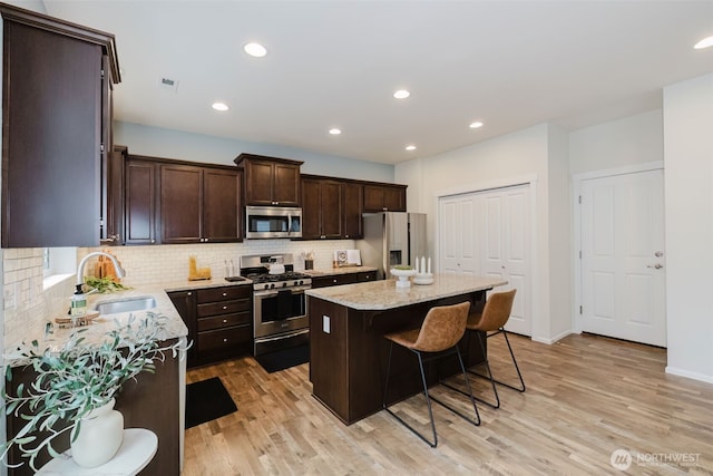 kitchen featuring dark brown cabinetry, stainless steel appliances, a kitchen island, a sink, and a kitchen bar