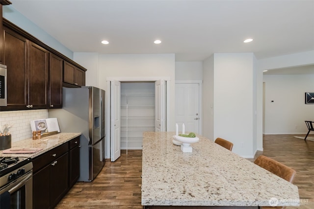 kitchen featuring dark wood-type flooring, a center island, light stone counters, and decorative backsplash