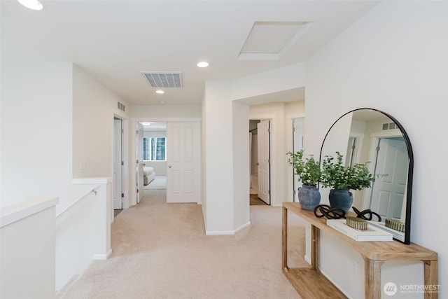 hallway with attic access, visible vents, baseboards, and light colored carpet