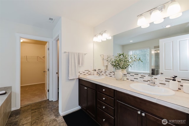 bathroom with a stall shower, a sink, backsplash, and double vanity