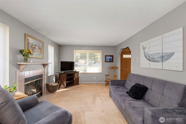 living area featuring baseboards, arched walkways, light colored carpet, and a tile fireplace