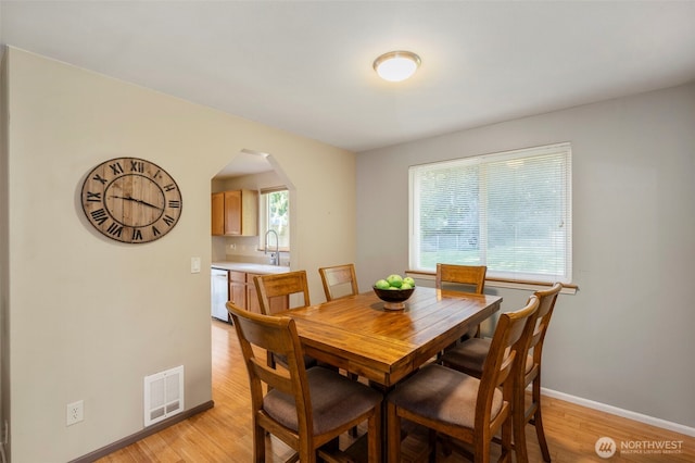 dining space with light wood-style flooring, visible vents, arched walkways, and baseboards