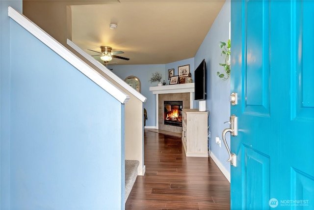 foyer with a ceiling fan, a tiled fireplace, dark wood finished floors, baseboards, and stairs