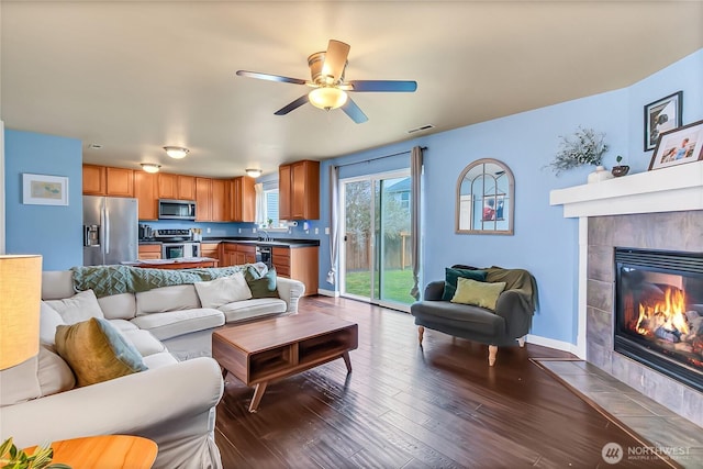 living room featuring visible vents, a ceiling fan, dark wood-style floors, baseboards, and a tile fireplace