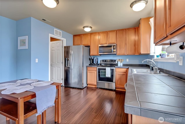 kitchen with visible vents, a sink, dark wood-style floors, tile countertops, and stainless steel appliances