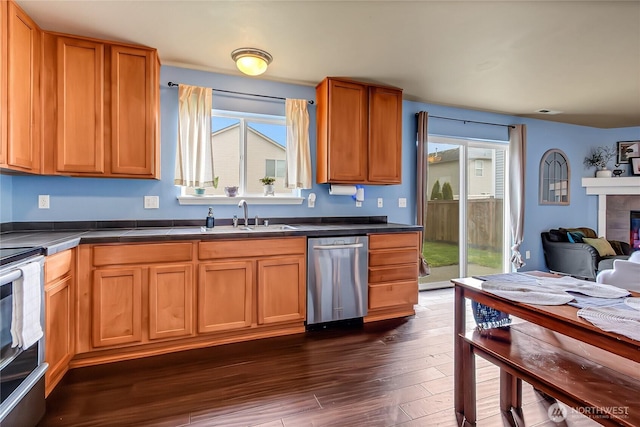 kitchen with dark countertops, a tiled fireplace, stainless steel dishwasher, electric stove, and a sink