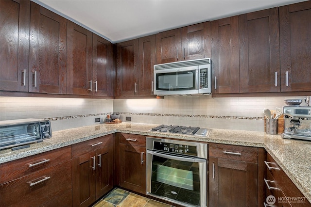 kitchen with dark brown cabinetry, tasteful backsplash, a toaster, light stone countertops, and stainless steel appliances