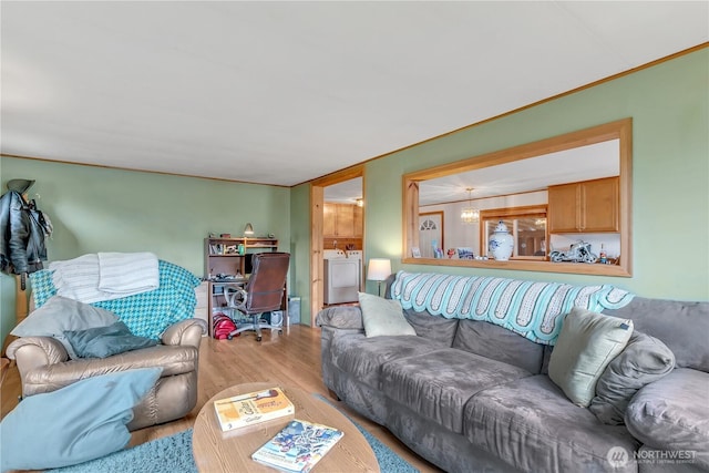 living area featuring ornamental molding, an inviting chandelier, wood finished floors, and washer and dryer