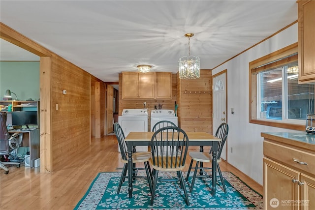 dining room featuring washing machine and clothes dryer, light wood finished floors, an inviting chandelier, ornamental molding, and wooden walls