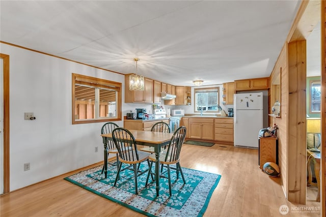 dining space with ornamental molding, an inviting chandelier, and light wood-style floors