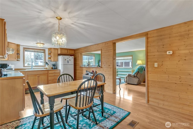 dining space with light wood-style floors, visible vents, a notable chandelier, and wooden walls