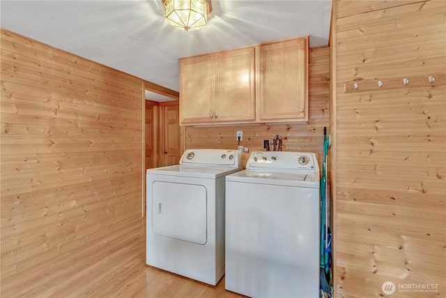 clothes washing area featuring washer and dryer, cabinet space, wood walls, and light wood finished floors