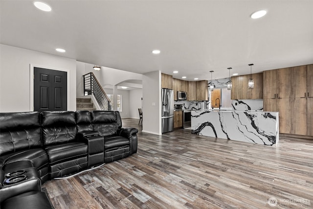 living area with baseboards, arched walkways, wood finished floors, stairs, and recessed lighting