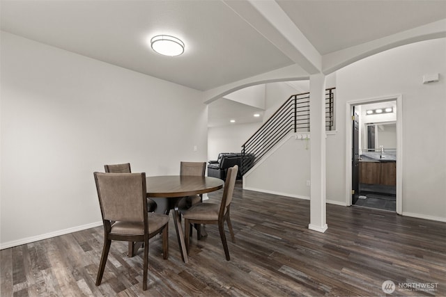 dining room with dark wood-style floors, arched walkways, and baseboards