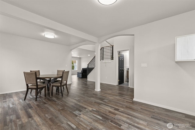 dining room with arched walkways, stairway, dark wood-style floors, and baseboards