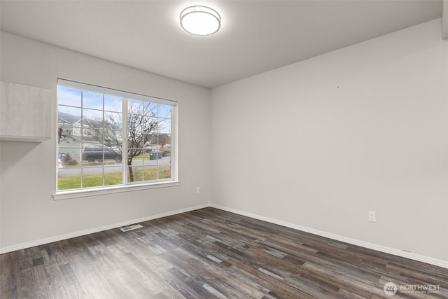 empty room featuring dark wood-style floors, visible vents, and baseboards