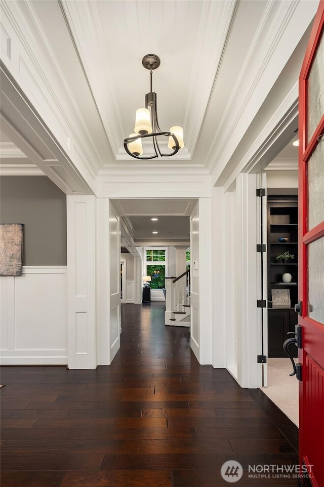 foyer with a chandelier, crown molding, dark wood finished floors, stairway, and a wainscoted wall