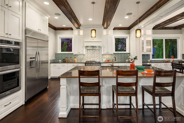 kitchen with stainless steel appliances, dark countertops, beamed ceiling, a sink, and dark wood finished floors