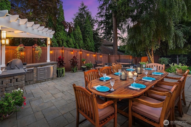 view of patio with exterior kitchen, a fenced backyard, outdoor dining space, and grilling area