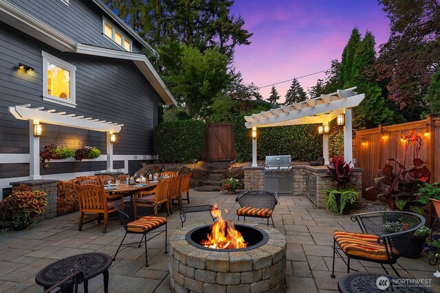 view of patio with an outdoor fire pit, a pergola, an outdoor kitchen, a fenced backyard, and outdoor dining space