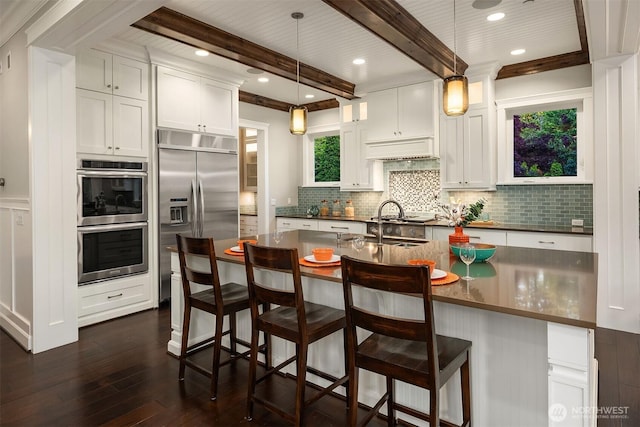 kitchen with dark countertops, appliances with stainless steel finishes, dark wood finished floors, backsplash, and beam ceiling