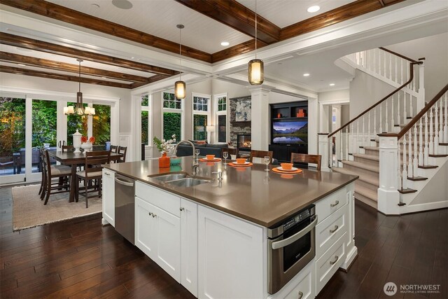 kitchen featuring a sink, stainless steel appliances, open floor plan, dark wood finished floors, and a glass covered fireplace