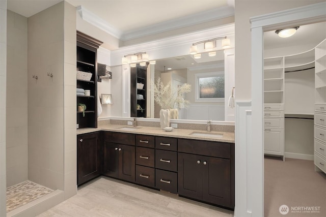 full bath featuring crown molding, double vanity, a tile shower, a walk in closet, and wood finished floors