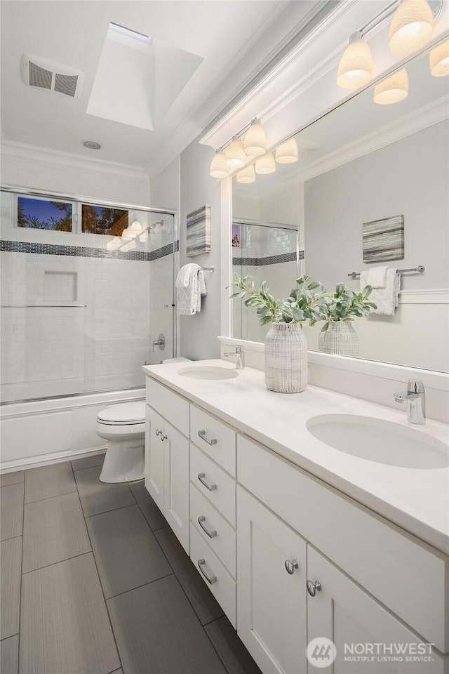 bathroom featuring ornamental molding, double vanity, toilet, enclosed tub / shower combo, and tile patterned flooring