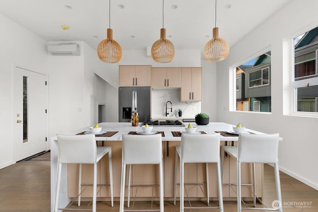 kitchen with pendant lighting, stainless steel refrigerator with ice dispenser, an AC wall unit, and light brown cabinetry