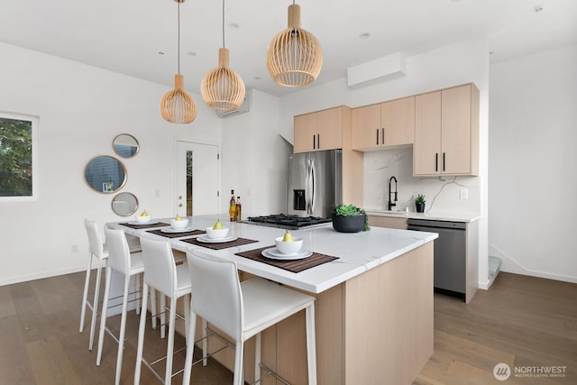 kitchen featuring a kitchen island, appliances with stainless steel finishes, hanging light fixtures, light brown cabinets, and a sink