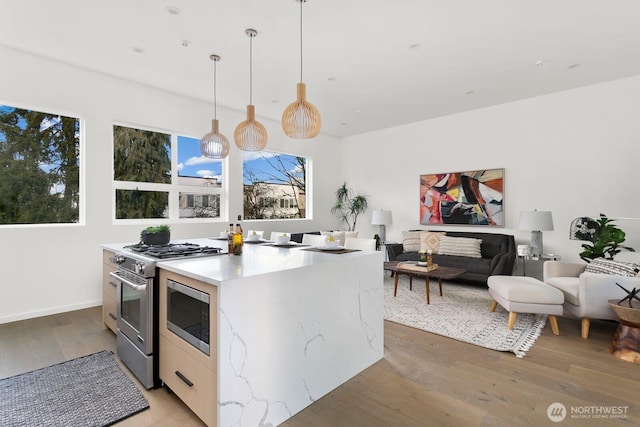 kitchen with open floor plan, light countertops, light wood-type flooring, stainless steel range with gas cooktop, and decorative light fixtures