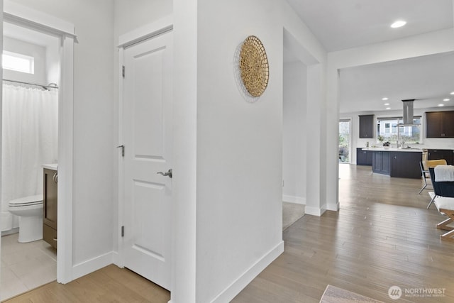 corridor featuring light wood finished floors, recessed lighting, and baseboards